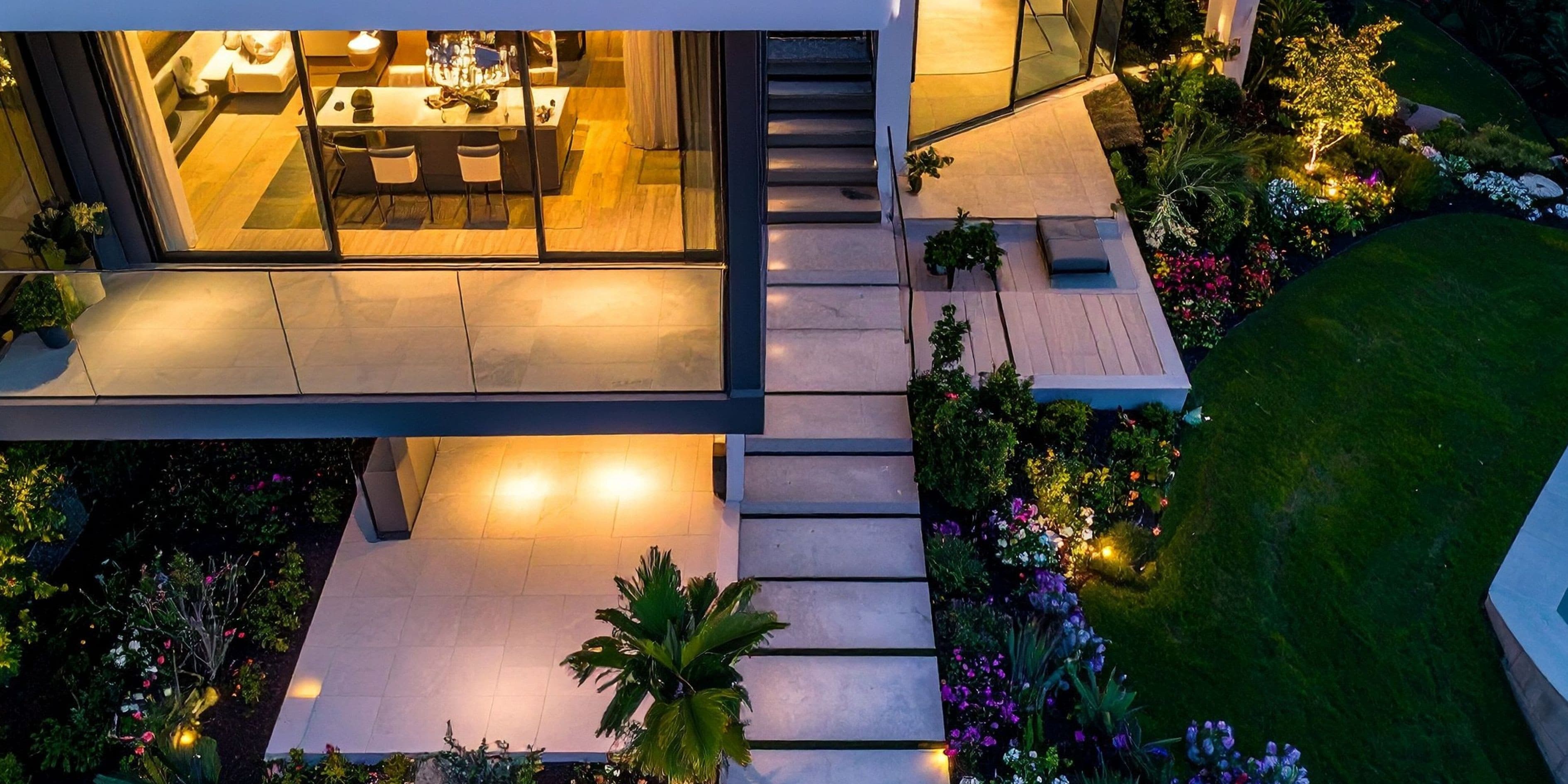 Luchtfoto in de avond van een moderne woning met verlicht natuurstenen terras, trap en beplante border